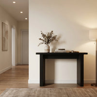 Black ribbed-leg console table styled in a warm hallway with dried eucalyptus, stacked books, and soft floor lamp light