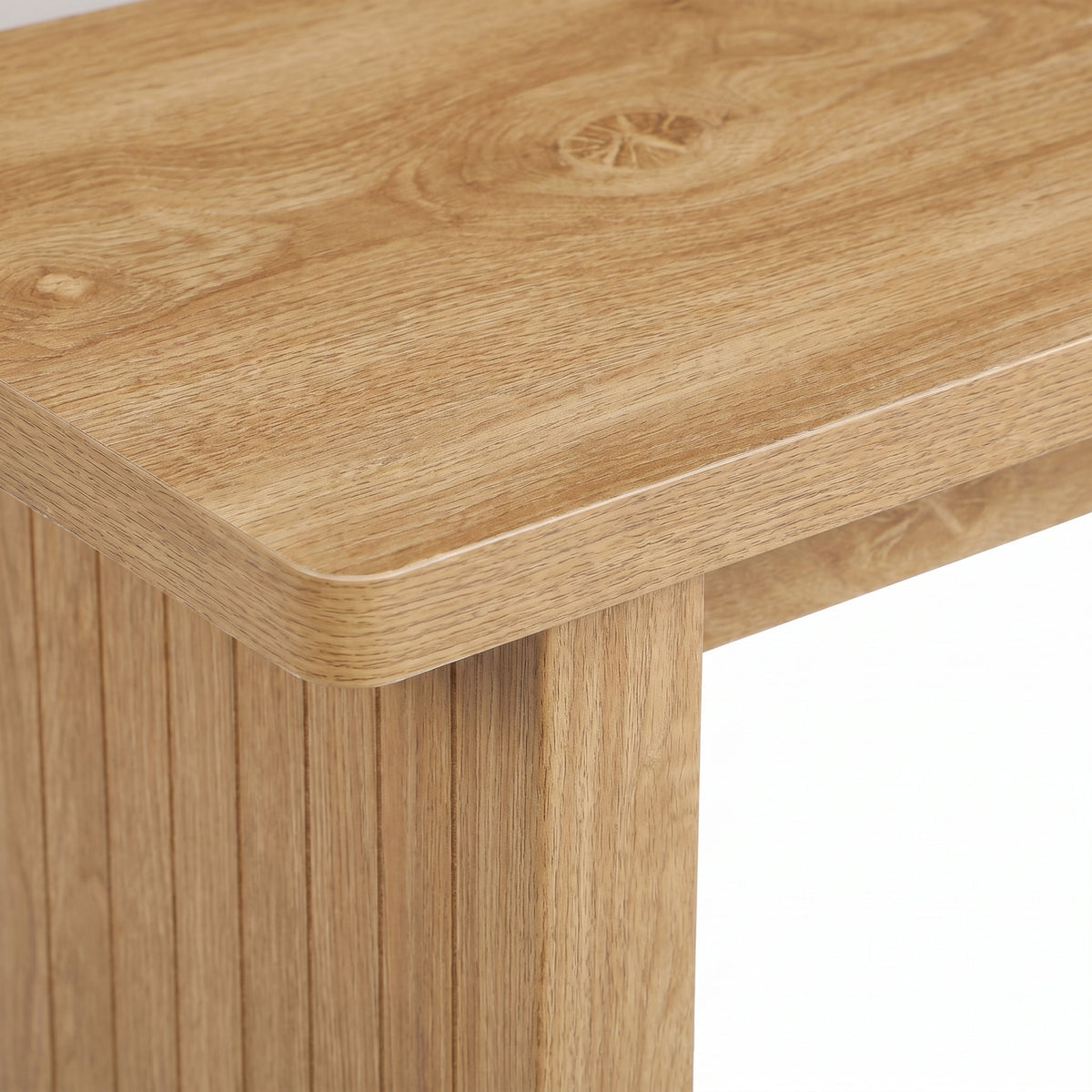 Close-up of light oak table corner showing rounded edge, visible wood grain, knot detail, and vertical ribbed leg panel below