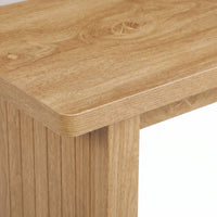 Close-up of light oak table corner showing rounded edge, visible wood grain, knot detail, and vertical ribbed leg panel below