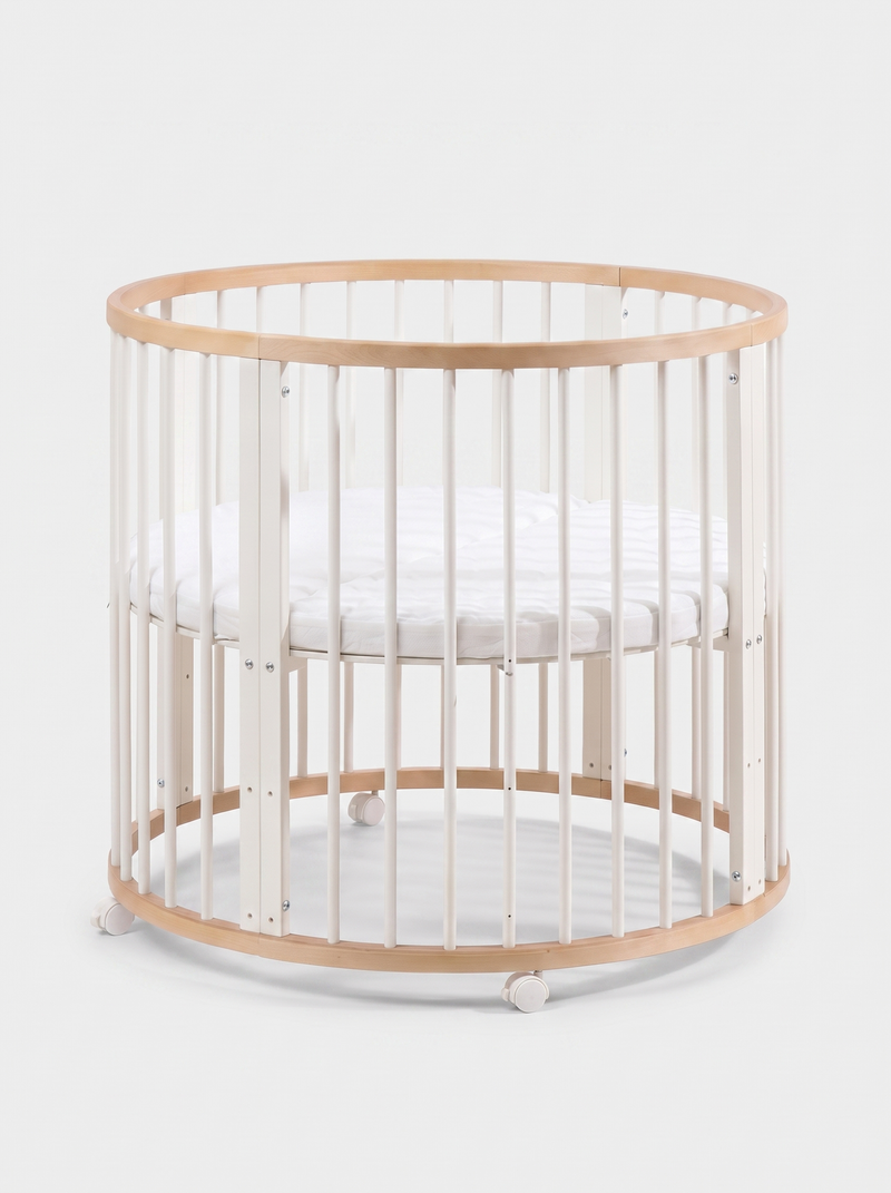 Round wooden baby playpen with white vertical slats, natural wood rim and base ring, white mattress inside, on lockable ca…