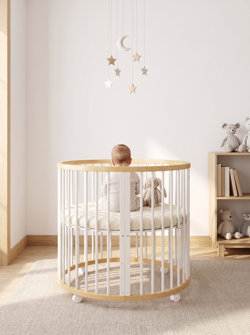 Round wooden playpen with white slats, baby sitting inside facing away, star mobile above, soft toys and bookshelf in nurs…
