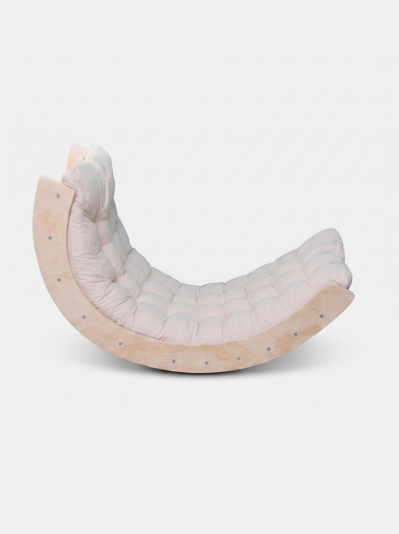 Pale pine rocker arch with white tufted cushion fitted inside, side-angle view showing curved wood frame and button detail…