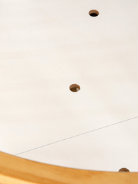 Close-up of white playpen base showing two brown cork screw-hole plugs on the surface, with natural wood rim visible at bo…