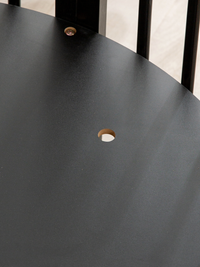 Close-up of matte black round tabletop surface with central umbrella hole and visible fixing screw, black slat frame behind