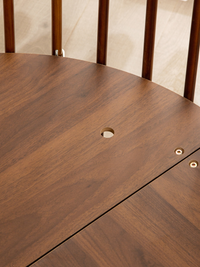 Close-up of dark walnut-stained round playpen top surface showing central cable hole and two brass screw fixings at extens…