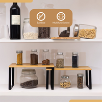 Two bamboo-top black metal cabinet risers holding spice jars on upper tiers, with glass storage jars underneath, on a whit…
