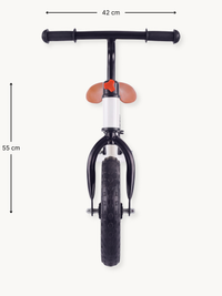 Front view of white balance bike showing 42 cm handlebar width and 55 cm height, black grips, tan saddle, knobbed front tire