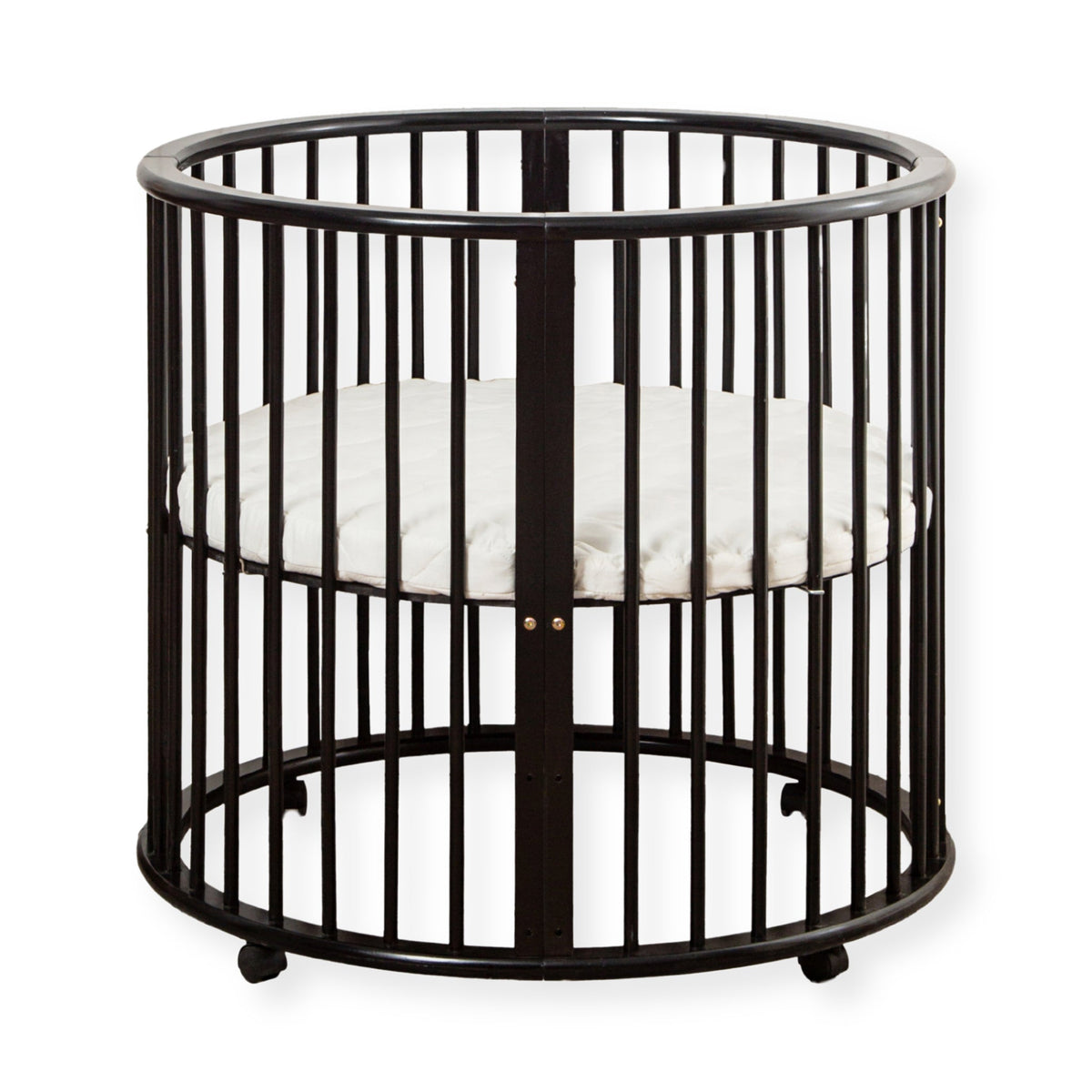 Black round wooden baby playpen with vertical spindles, white round mattress inside, and small wheels on base, white backg…