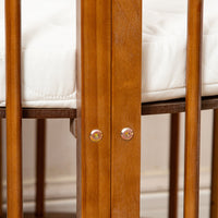 Close-up of two gold bolt fixings on a walnut-finish wooden baby playpen post, white quilted mattress visible above