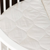 Close-up of cream quilted mattress surface inside a dark and white wooden baby playpen, showing circular stitching pattern…