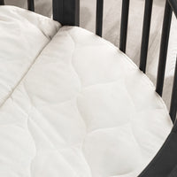 White quilted oval mattress fitted inside a black round wooden playpen, angled top-down view showing stitched pattern detail
