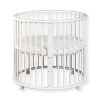White round wooden baby playpen with vertical slats, circular mattress inside, and four castors, front view on white backg…